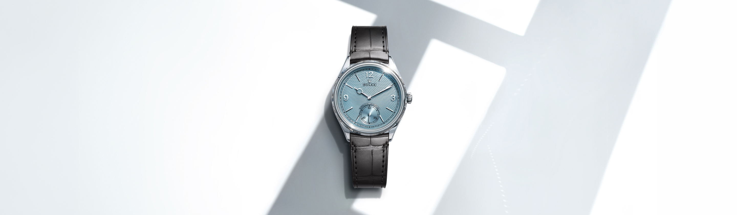 Rolex Perpetual 1908 in platinum with ice blue guilloché dial and gray alligator strap against angular light backdrop