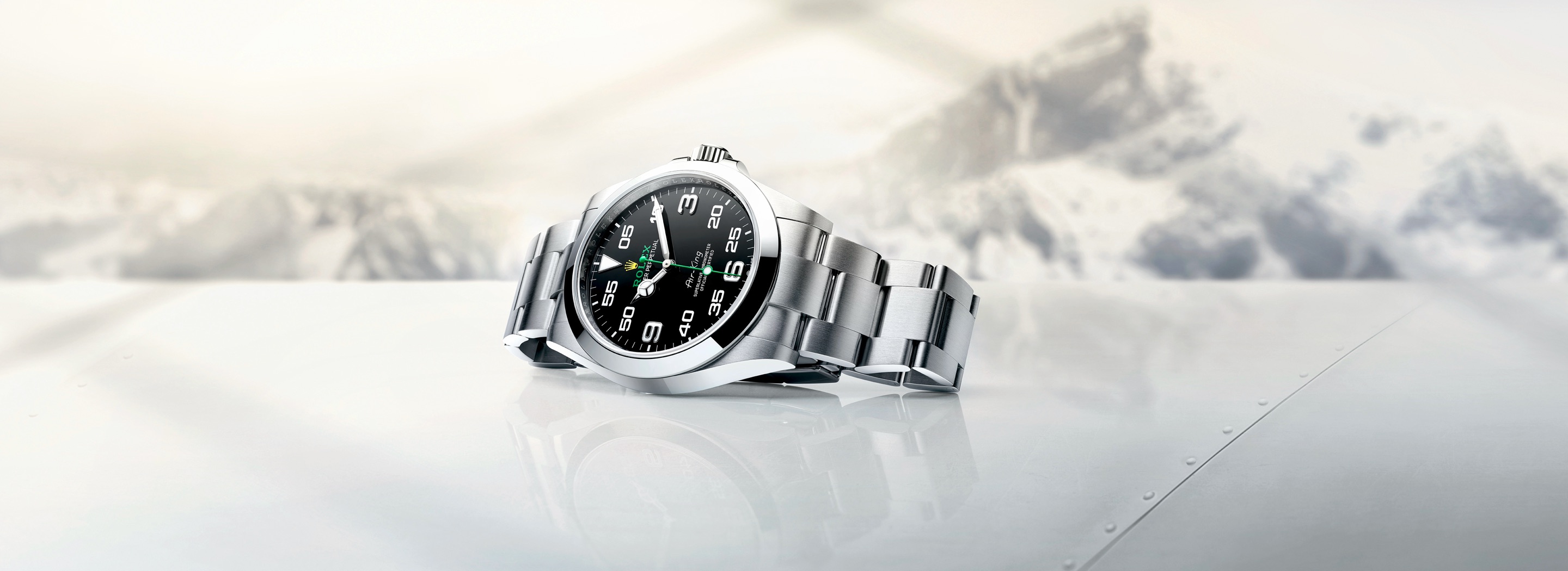 Rolex Air-King in Oystersteel resting on a reflective aircraft wing surface with snow-capped mountain backdrop