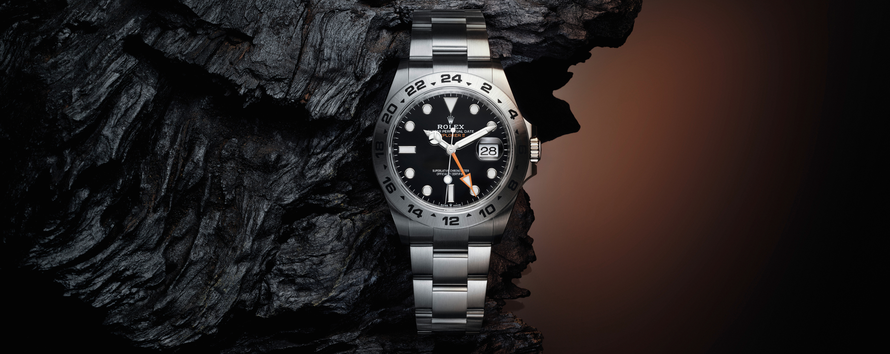 Rolex Explorer II in Oystersteel with black dial nestled in dark volcanic rock with warm brown backdrop