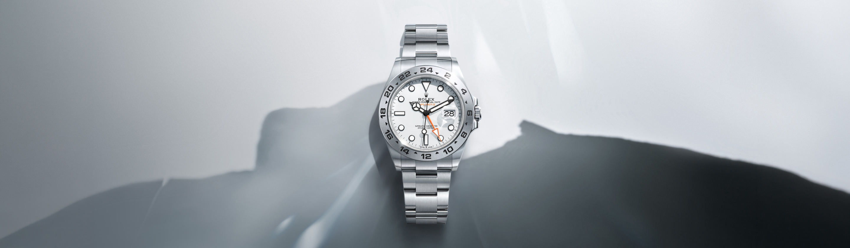 Rolex Explorer II in Oystersteel with white dial and 24-hour bezel against abstract mountain shadow backdrop