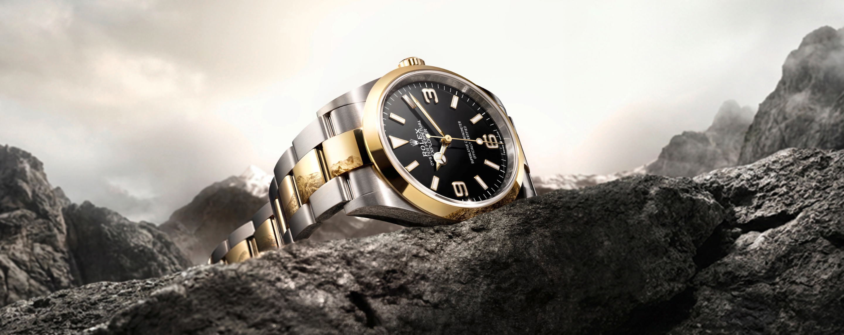 Rolex Explorer 36 in yellow Rolesor resting on rocky mountain summit with dramatic cloudy sky