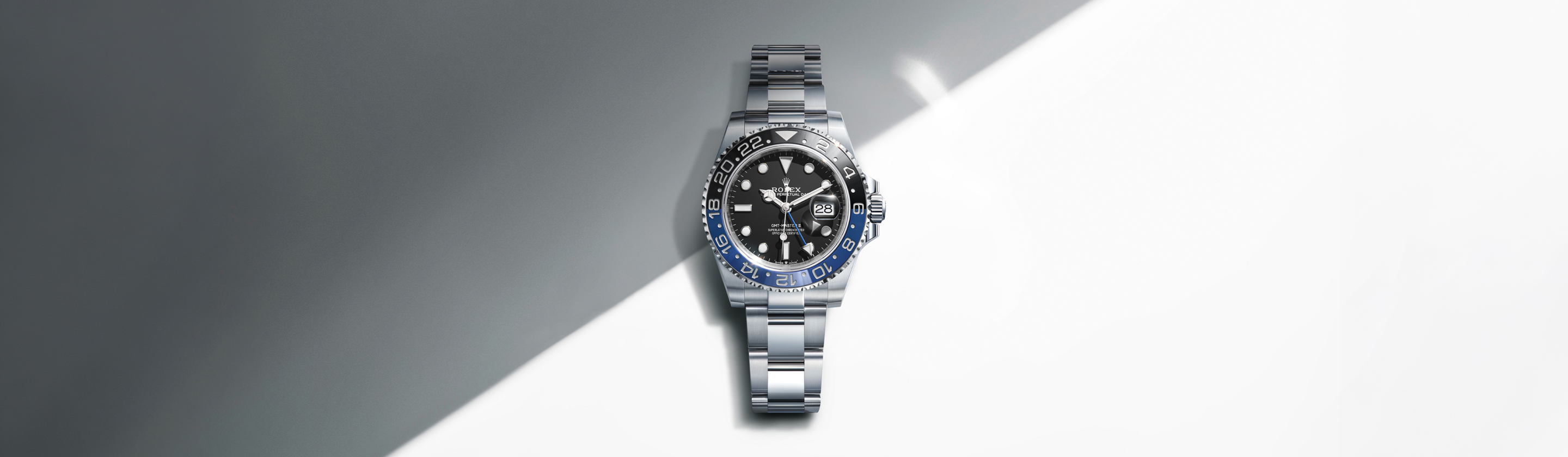 Rolex GMT-Master II in Oystersteel with black dial and blue-black Cerachrom bezel on an Oyster bracelet, against a grey and white geometric background