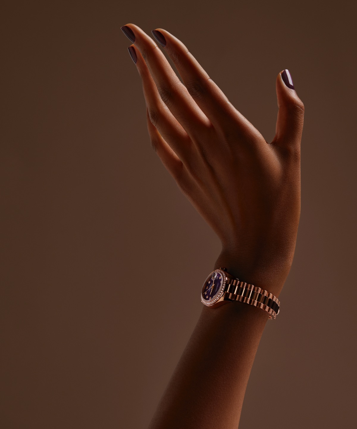 Rolex Lady-Datejust in Everose gold with violet dial and diamond-set bezel on a President bracelet, worn on a raised wrist against a warm brown background