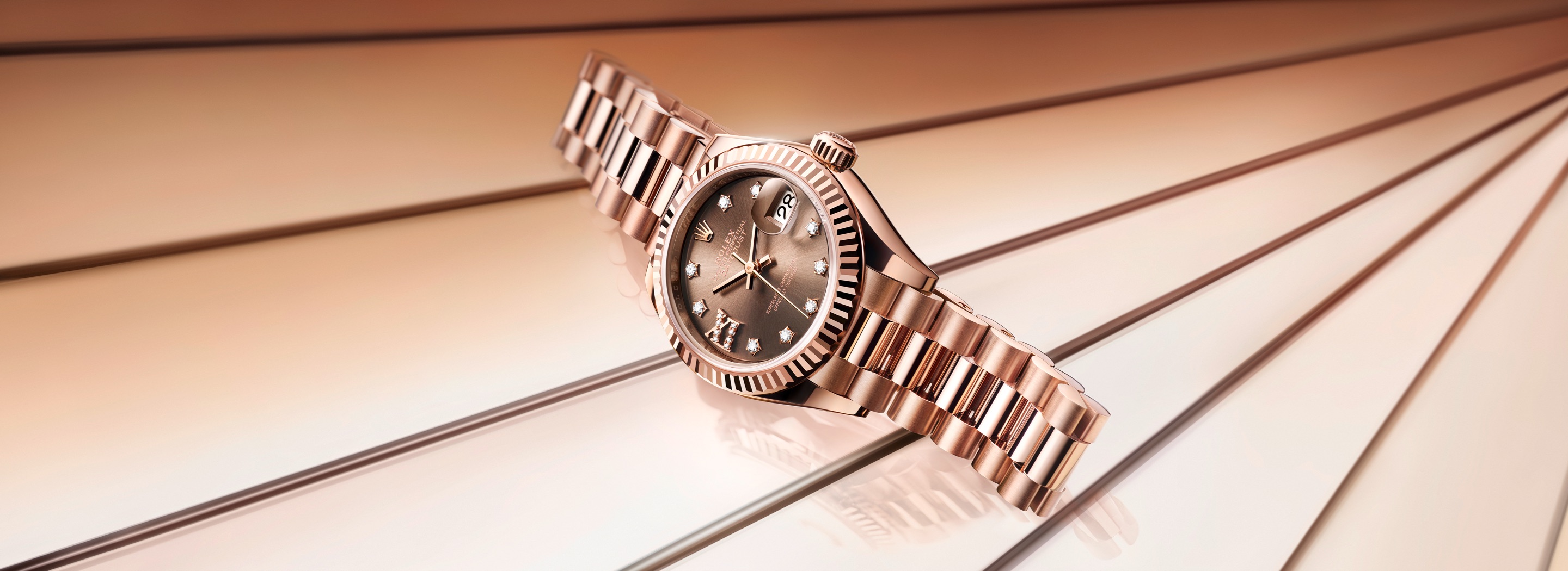 Rolex Lady-Datejust 28 in Oystersteel with pink sunray dial and domed bezel on an Oyster bracelet, set against soft pink flowing fabric