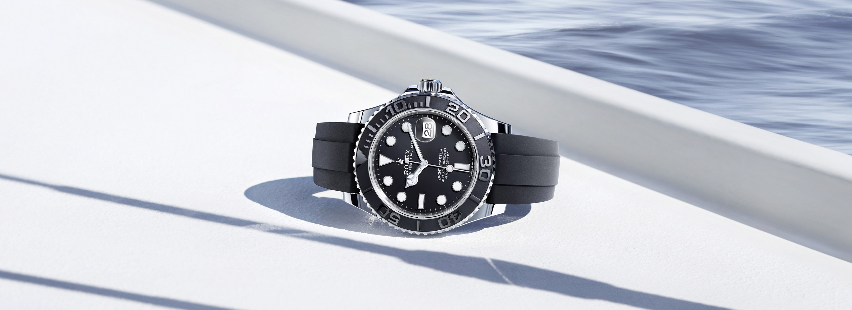 Rolex Yacht-Master 42 in white gold with black dial and Oysterflex bracelet, side profile against ocean backdrop