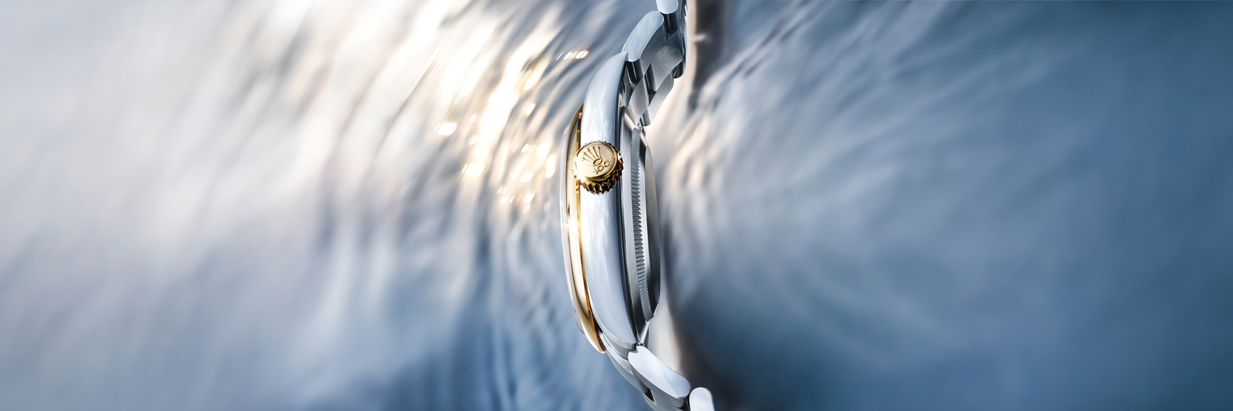 Rolex Oyster Perpetual 41 in yellow Rolesor, side profile detail of yellow gold winding crown and case against rippling water